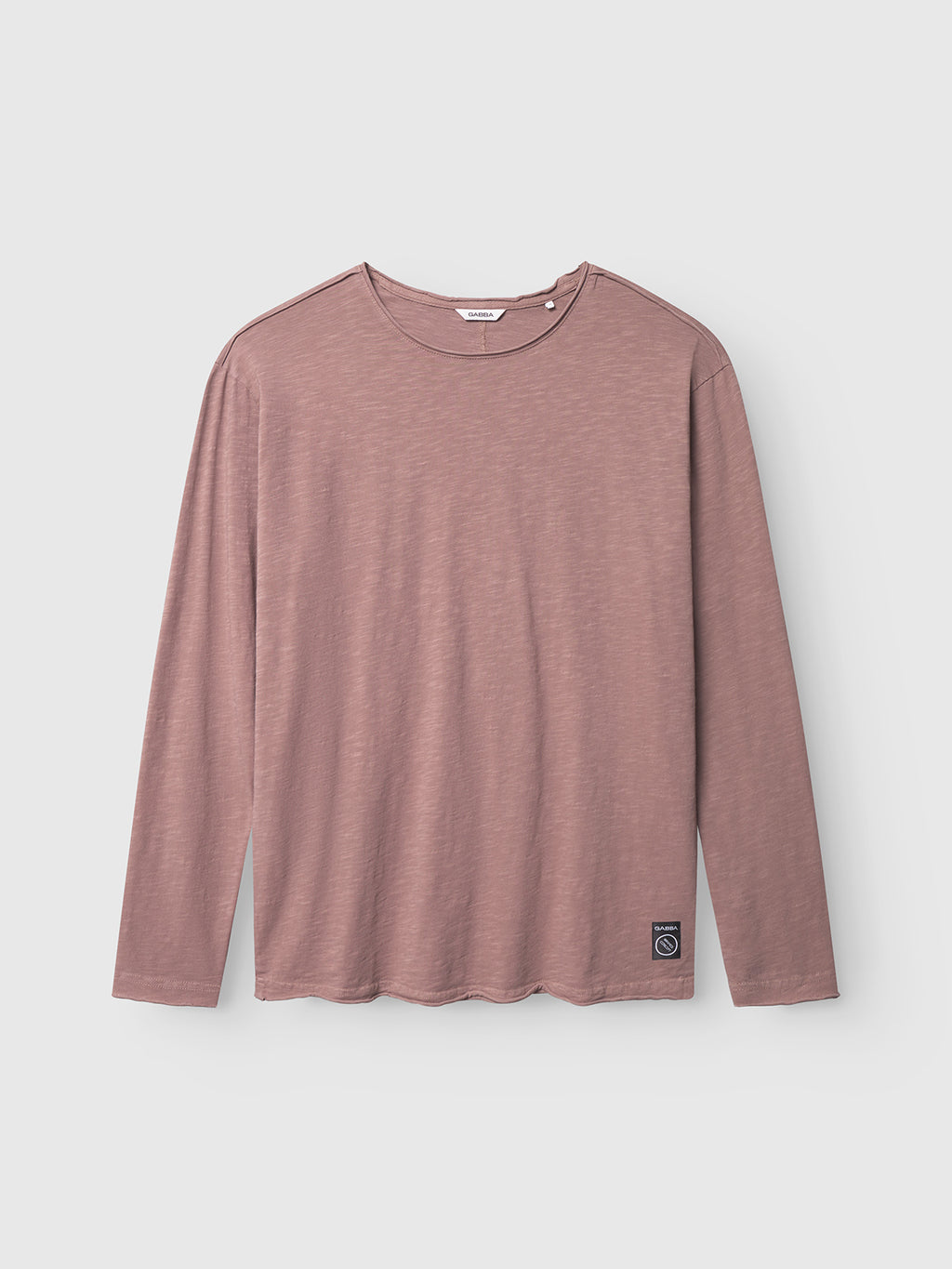 The Gabba Paros Rif GWC - Rose is a mauve long sleeve t-shirt with a subtle textured fabric and faded look, shown flat on a light gray background. A small rectangular patch is sewn near the bottom hem on one side.