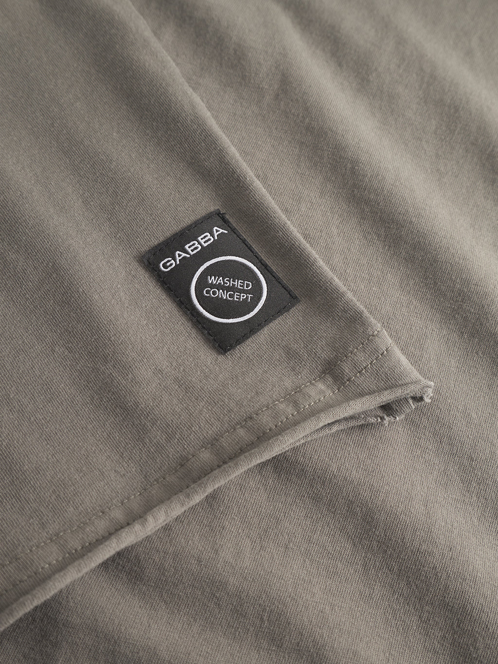 Close-up of a folded grey Idra Rig GWC cotton fabric by Gabba, featuring a small black rectangular label stitched on the surface that reads Gabba and Washed Concept.
