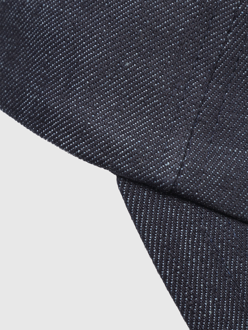 Close-up of the Sity Self Cap - Dark Denim by Gabba, crafted from recycled fibers. Overlapping pieces reveal visible weave texture and diagonal stitching on deep blue denim, set against a white background.