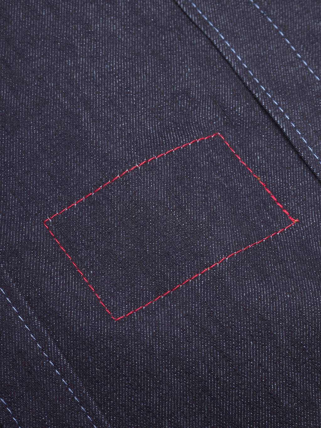 Close-up of the Gabba Bag Self in dark blue denim, showcasing visible blue stitching and a rectangular patch with red thread outlining a contrasting hand-stitched repair inspired by authentic Japanese craftsmanship.
