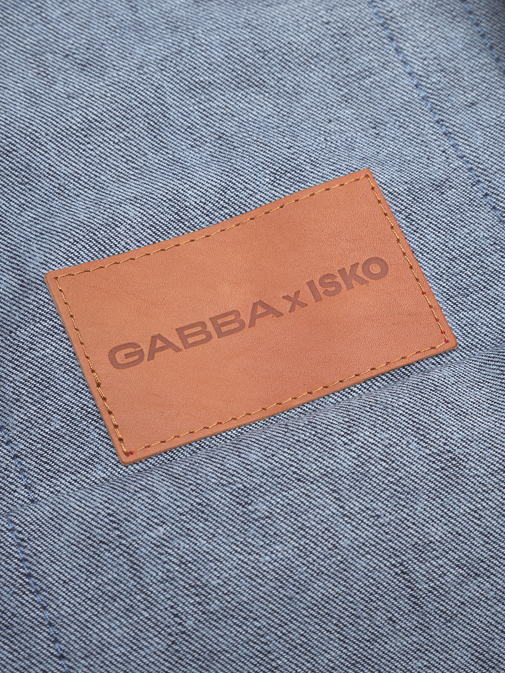 A close-up of a brown leather patch stitched onto Bag Self - Dark Blue Denim by Gabba, made from recycled fibers, with GABBA x ISKO printed on the patch.