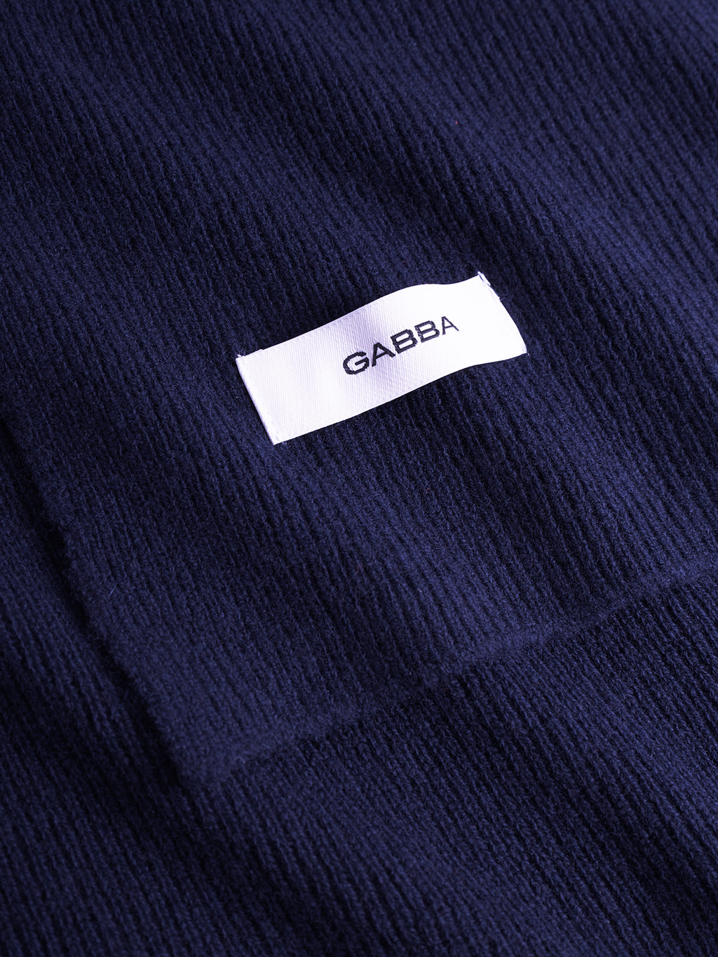 Close-up of the Biwa Aico - Navy ribbed knit scarf by Gabba, featuring a white rectangular label with Gabba in black text.