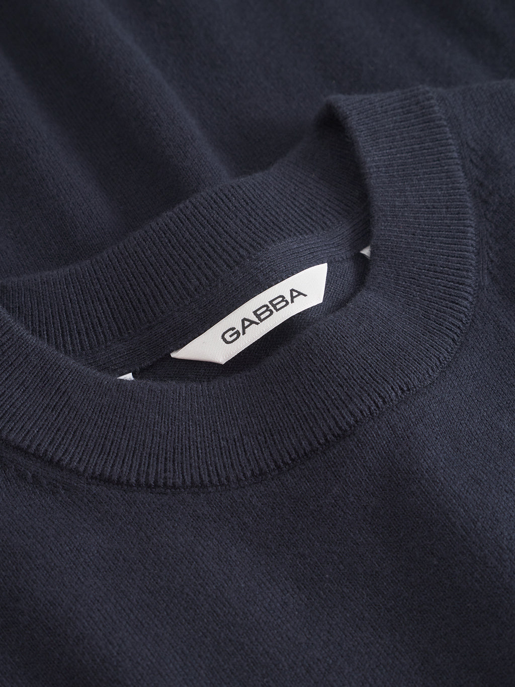 A close-up of the Gabba Amori Prex LS - Navy sweater shows its dark navy knitwear, ribbed crew neck, and a white inner collar label with Gabba in bold black letters.