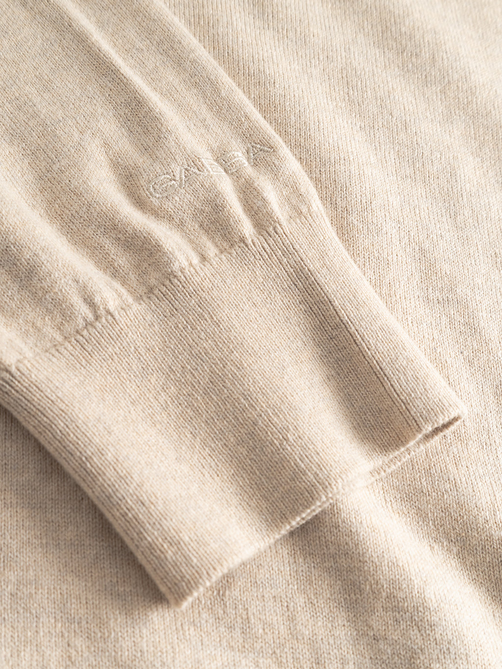A close-up of the Gabba Amori Prex LS - Sand sweater sleeve highlights its fine texture, ribbed cuffs, and subtle embroidered lettering near the wrist.