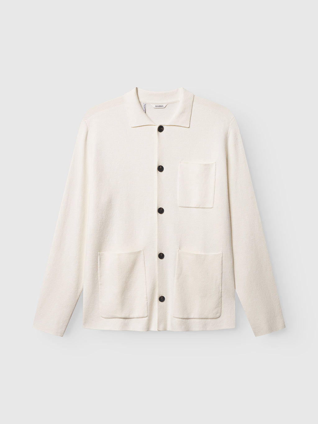 The Gabba Blanko New Cardi LS in off white features long sleeves, a collared button-up design, and three front pockets. Minimalist and ideal for layering, it's shown against a light gray background.