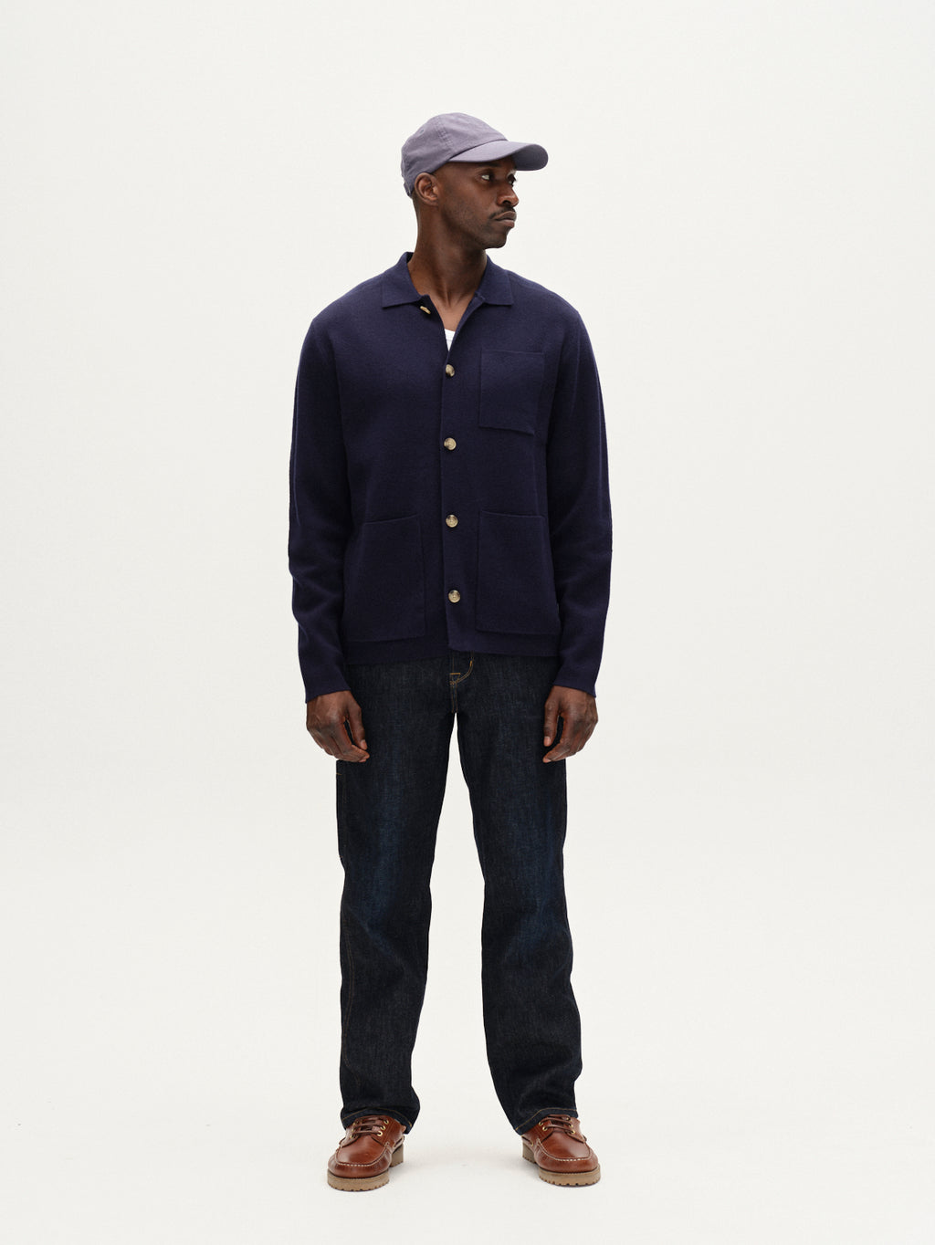 Man wearing a navy jacket, jeans, and a cap on a white background