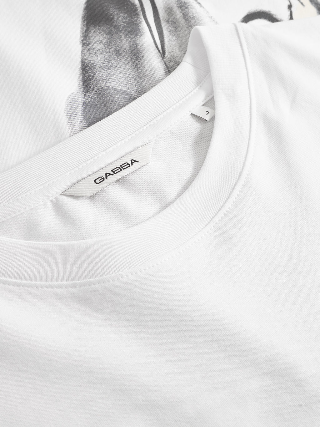 Close-up of the white Gabba Dune Kay Man Bauw SS GOTS T-shirt, made from GOTS-certified organic cotton, featuring a visible “Gabba” label inside the collar and a partial grey and black design on the shirt below.