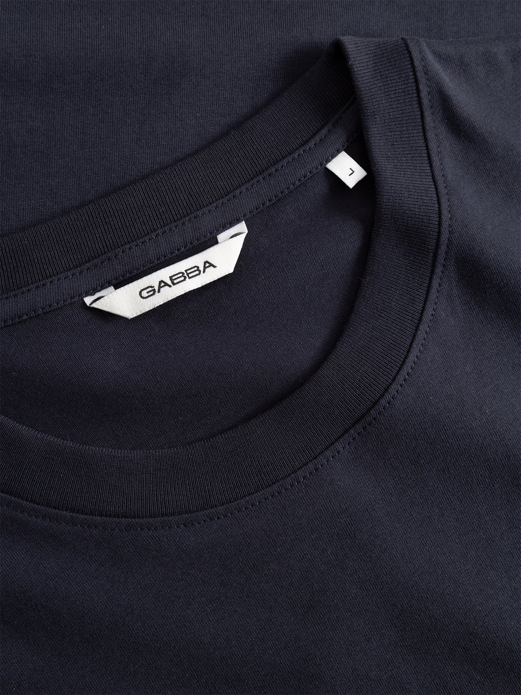 Close-up of a neatly folded Gabba Dune Kay Man Bauw SS GOTS - Navy organic cotton t-shirt, featuring a white Gabba label and a small J size tag near the collar.