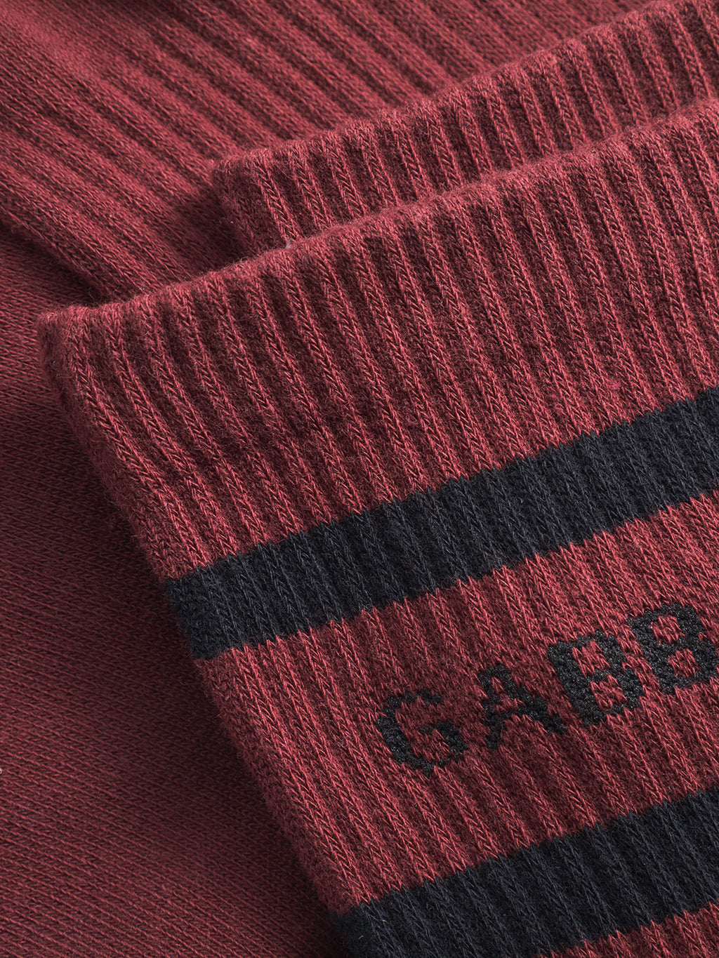 Close-up of red knitted fabric with black stripes and partial “GABBA” text, likely on Zino Socks - Red Russet by Gabba. The texture, ribbed cuffs, and premium comfort are clearly visible.