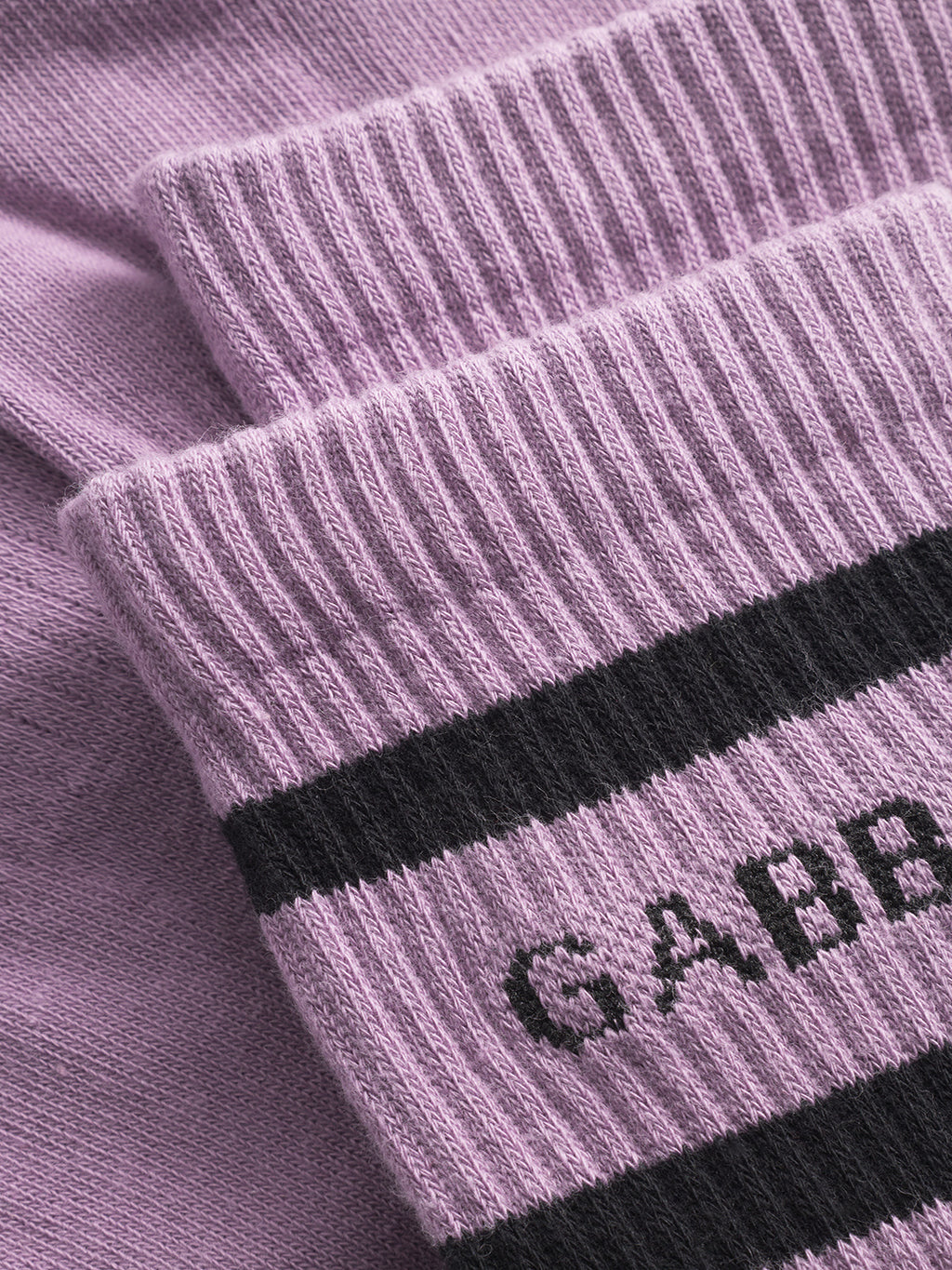 Close-up of Zino Socks - Dust Purple by Gabba: light purple cotton knit with ribbed cuffs, black stripes, and partially visible GABBA text. These breathable socks deliver premium comfort for everyday wear.