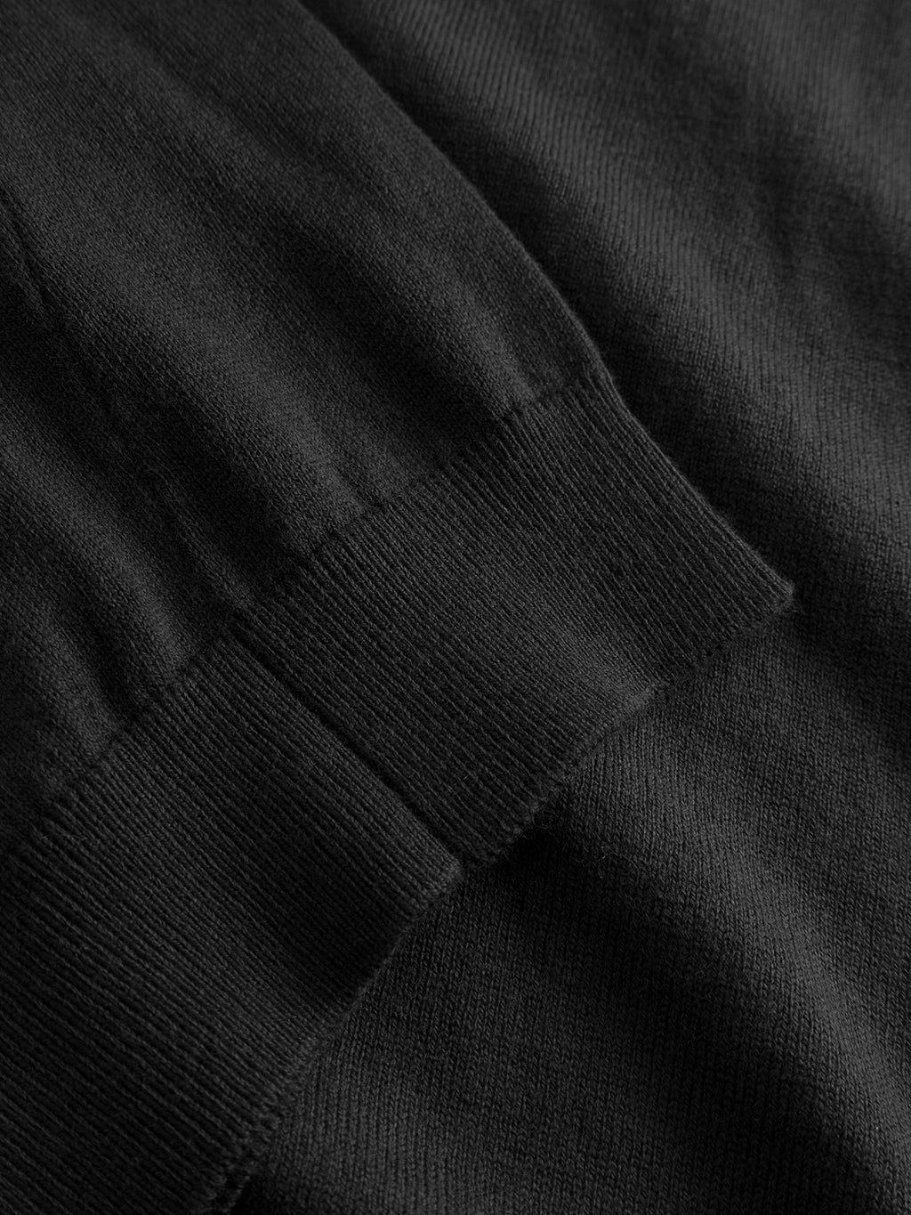 A close-up of black fabric shows the ribbed cuff and body of the Aris Prex - Black sweater by Gabba, highlighting its visible knit texture and soft material.