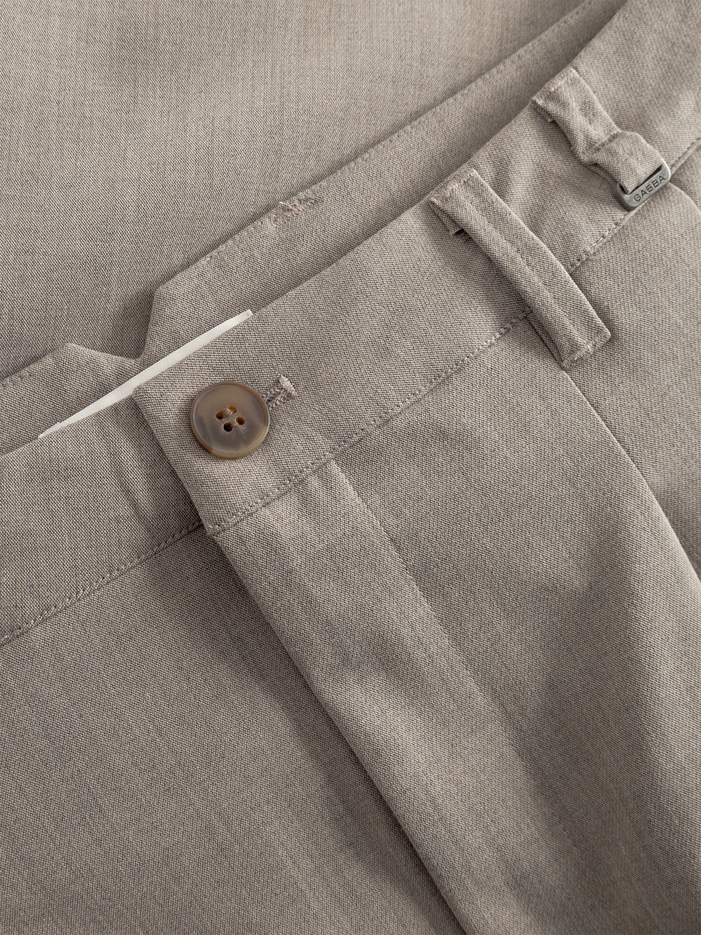 Close-up of Gabba Firenze Phin Cropped GRS trousers in Sand, featuring a brown button, belt loop, and waistband with visible tag. The fabric’s texture is clearly shown.