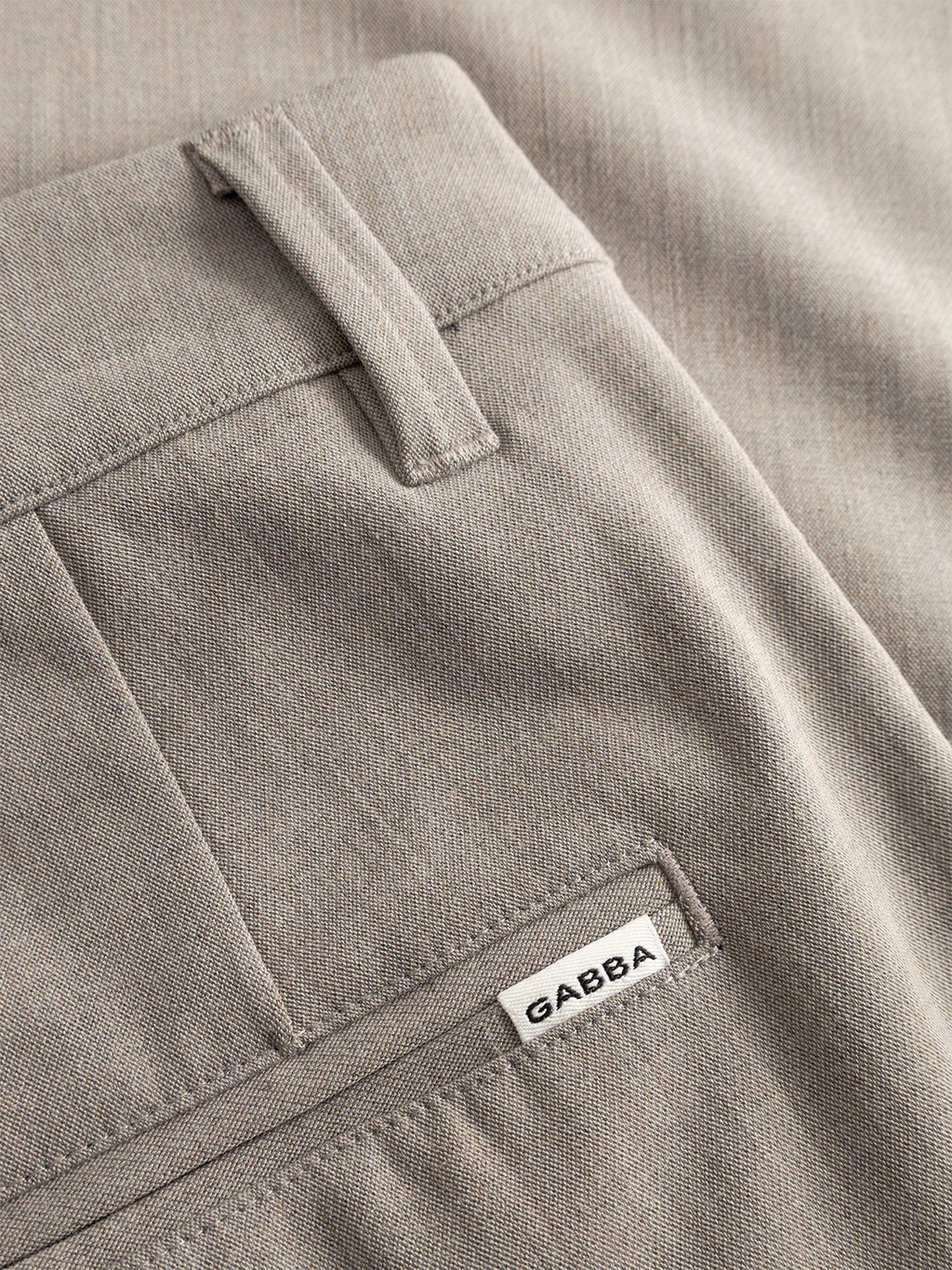 Close-up of Gabbas Firenze Phin Cropped GRS - Sand trousers featuring light brown fabric, a belt loop, back pocket, and a small white Gabba label sewn above the pocket.