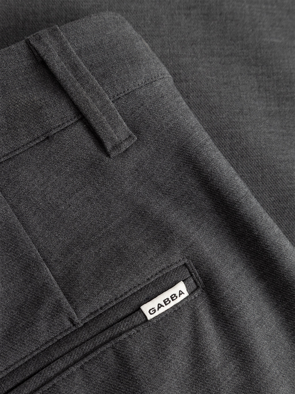 Close-up of Gabba Firenze Phin Cropped GRS trousers in dark grey. Features include a back pocket, belt loop, and a small white Gabba label near the pocket. The subtly textured fabric suits versatile formal looks.