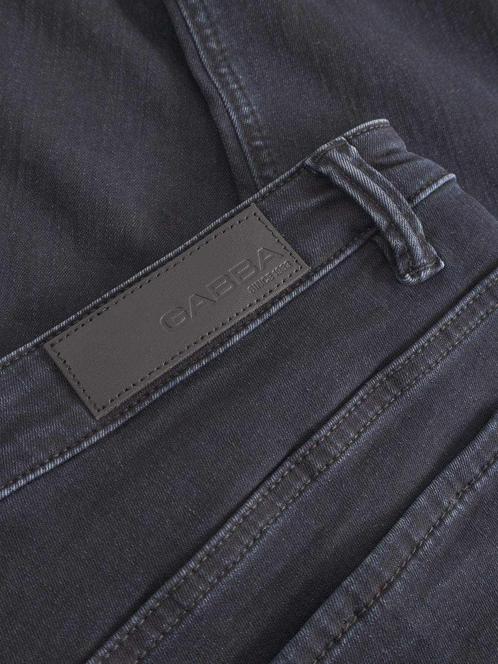Close-up of GABjones BlueBlack jeans from Gabba shows a black leather patch with embossed branding, visible stitching, and a slim straight fit designed for all-day comfort in blue-black denim.