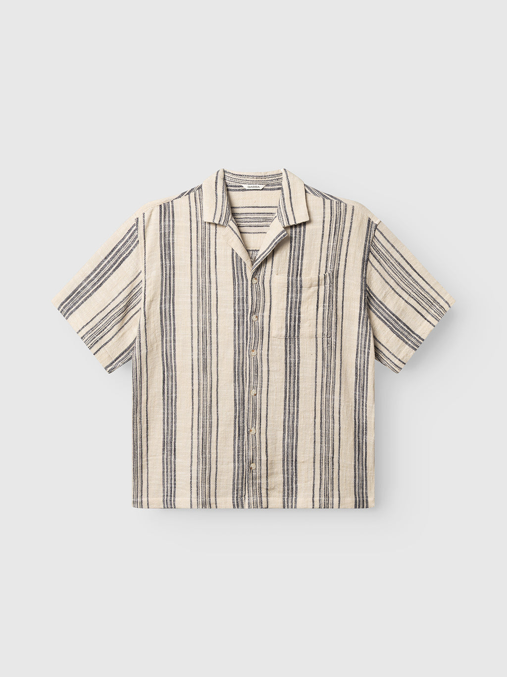 The GABjens Over Resort Riga SS Shirt by Gabba features navy and black stripes on beige fabric, a chest pocket, and an oversized, relaxed fit—ideal for casual resort wear.