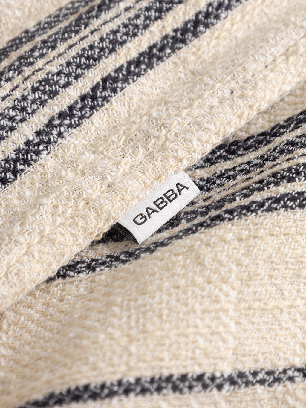 Close-up of the textured GABjens Over Resort Riga SS Shirt by Gabba in navy stripe slub cotton. A white tag with 
