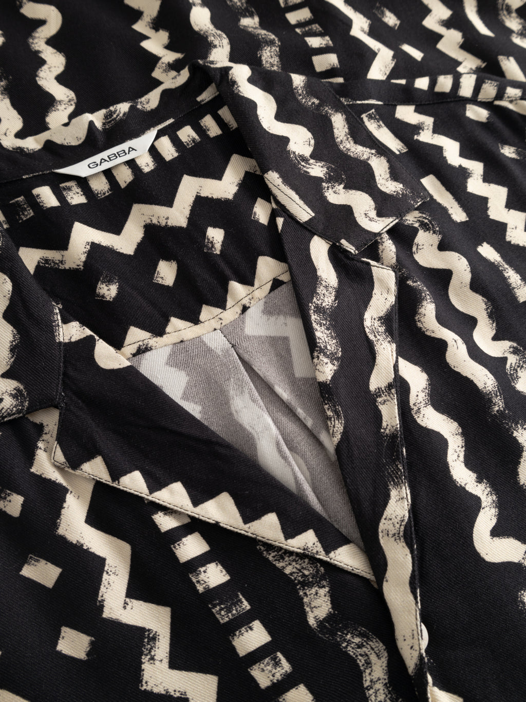 Close-up of the Gabba GABsven Reg Resort Oro SS Shirt - Multi Pattern, featuring an abstract geometric black and cream zigzag print, resort collar, visible Gabba label inside the neckline, and crafted from soft viscose twill.
