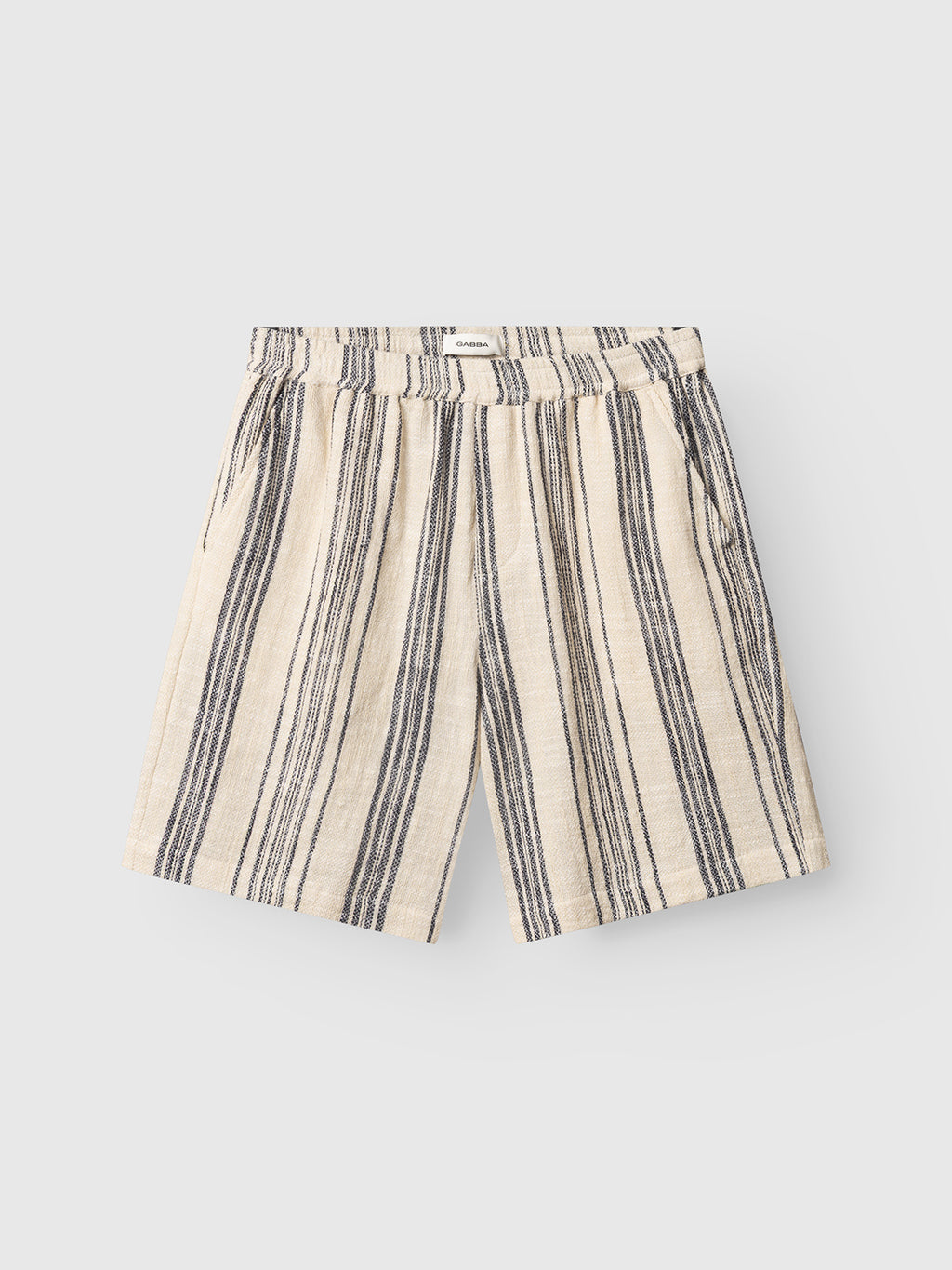 The Gabba GABtommi Riga Shorts - Navy Stripe are beige regular-fit shorts with vertical navy stripes, an elasticated waistband, and side pockets, shown laid flat on a light grey background.