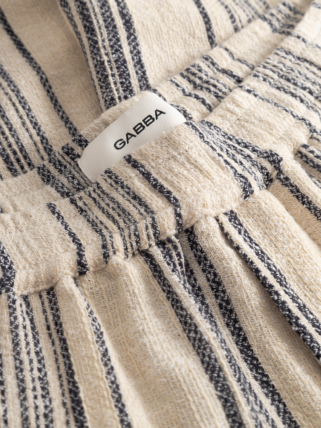 A close-up of Gabba's GABtommi Riga Shorts in navy stripe, featuring vertical stripes, an elasticated waistband, and a white GABBA label sewn into the waistband.