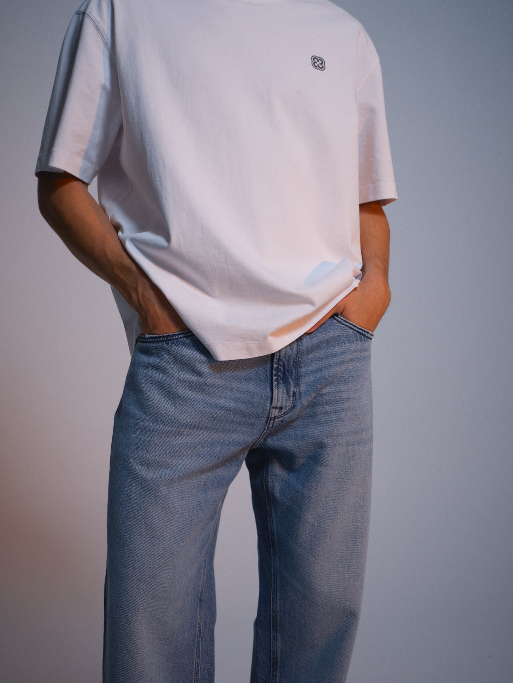 A person wearing the Gabba GABlegin Wix Chap Boxy Hour SS T-Shirt in white with a small chest logo and light blue jeans stands with hands in pockets. The image is cropped from shoulders to knees.