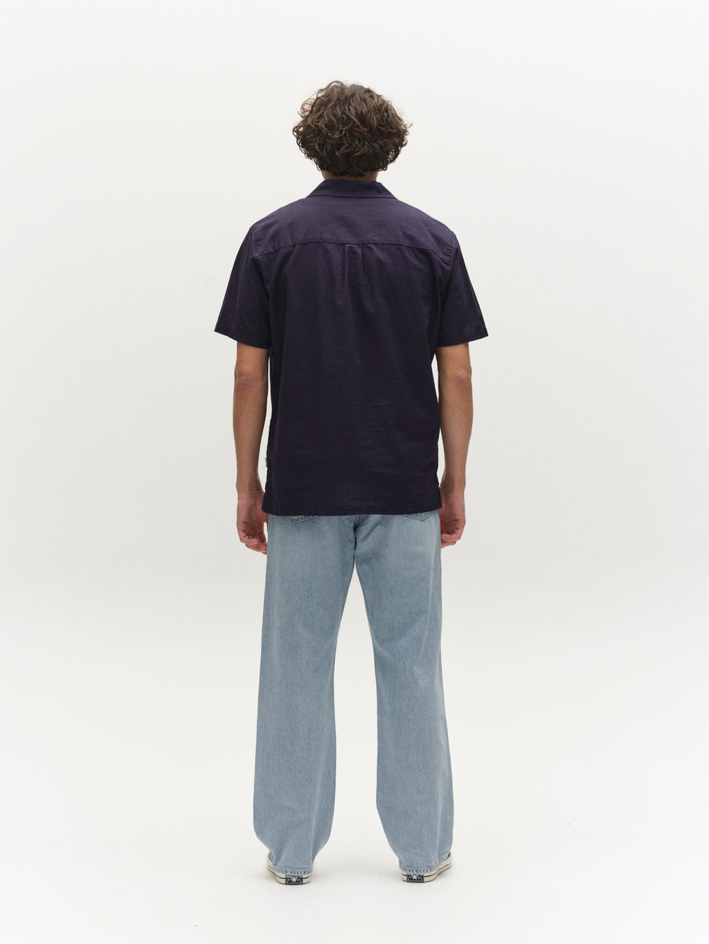 A person with curly hair faces away, wearing the Gabba GABtimo Resort Lins SS Shirt in navy and light blue jeans, set against a plain white background.