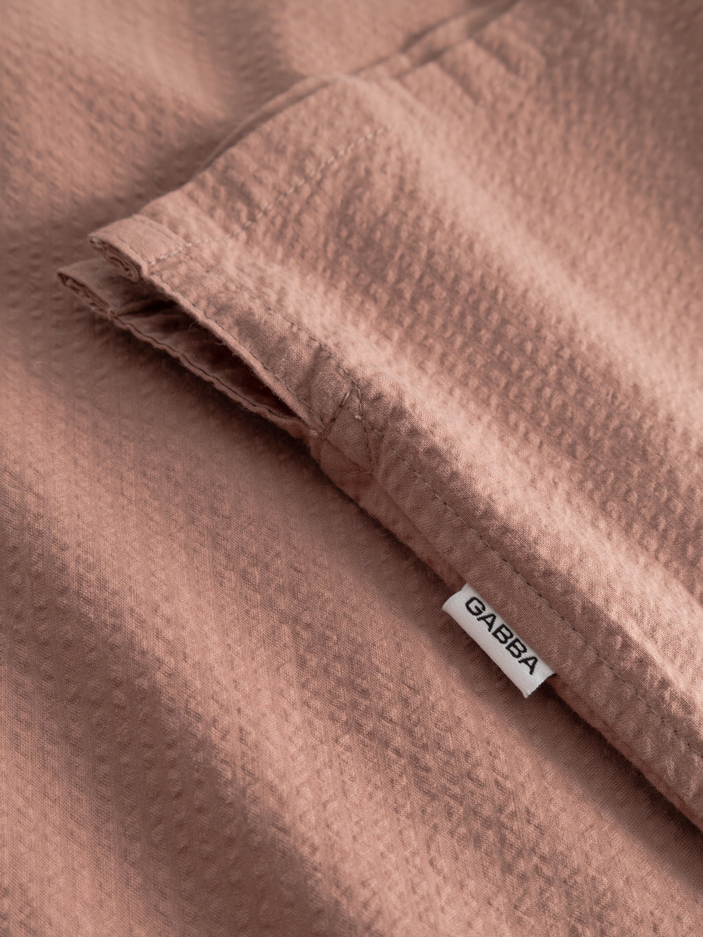 Close-up of the textured cotton seersucker fabric on the Gabba GABtimo Resort Ker SS Shirt in Wood Pink, featuring a small white Gabba tag near the seam.