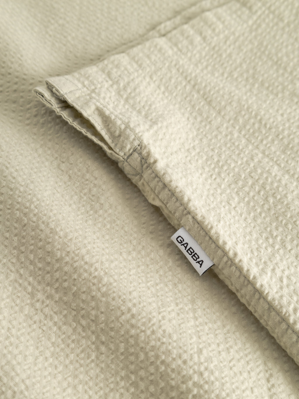 A close-up of the GABtimo Resort Ker SS Shirt in Alfa Green by Gabba, featuring textured seersucker fabric and a small white Gabba tag sewn into the seam—ideal for upscale short-sleeve resort style.