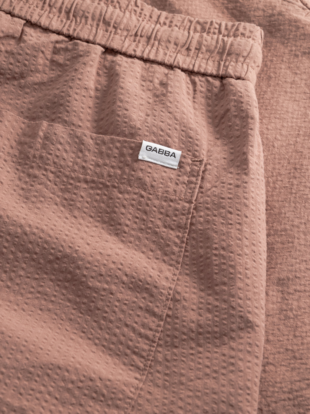 Close-up of Gabba GABtommi Ker Shorts in wood pink, made from textured fabric, featuring a regular fit, elastic waistband, and front pocket with a small white GABBA label above it.