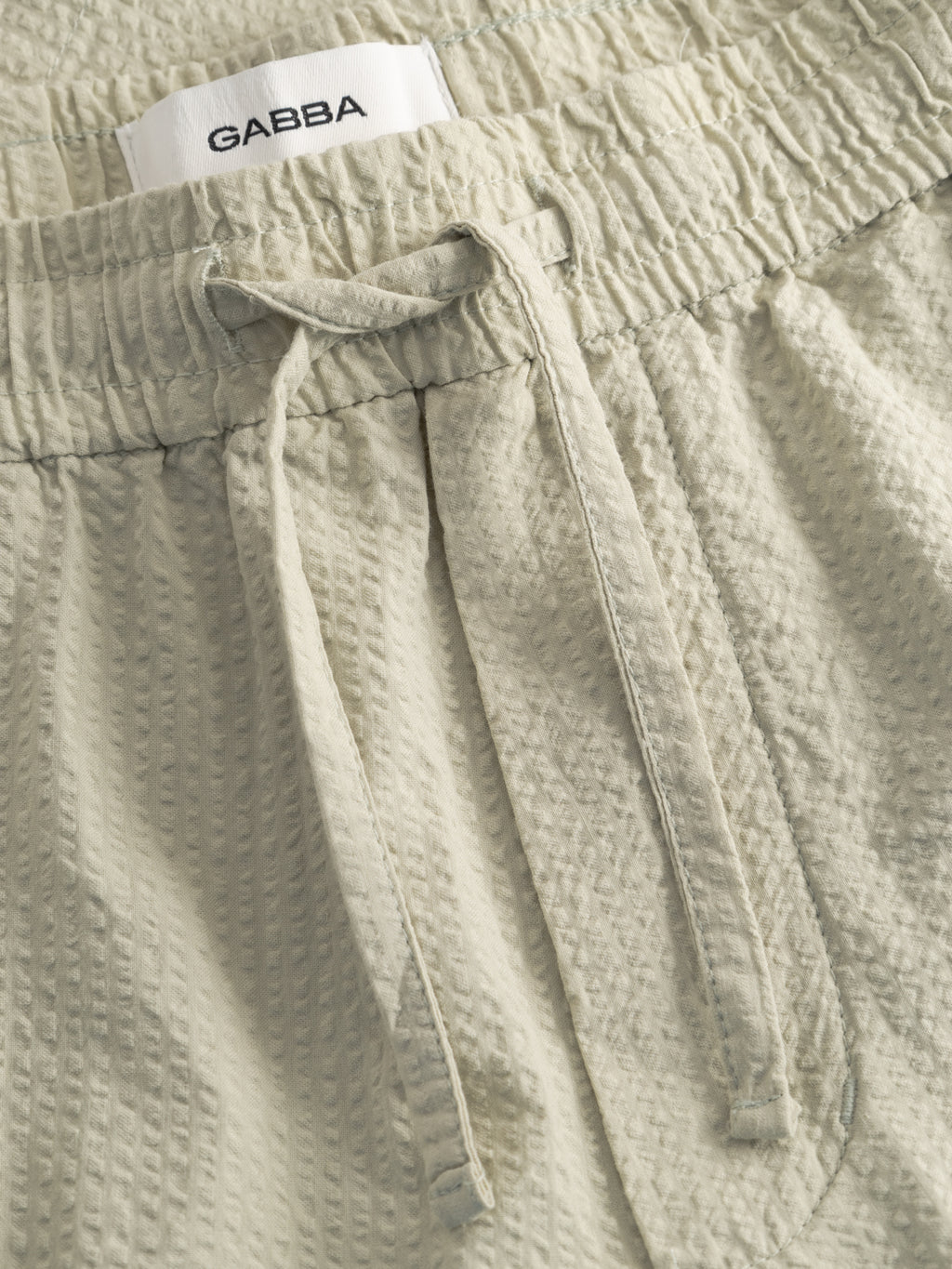 Close-up of Alfa Green textured GABtommi Ker Shorts by Gabba, featuring an elasticated waistband and a white GABBA label sewn inside.