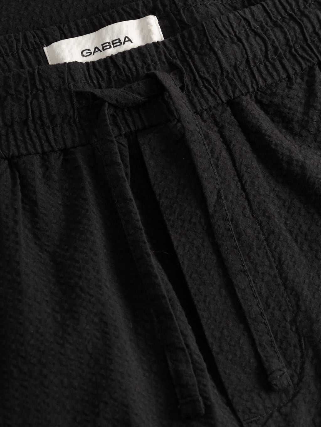 Close-up of black GABtommi Ker Shorts by Gabba, featuring a textured design, elasticated waistband, drawstring, and a white label with the Gabba brand name.
