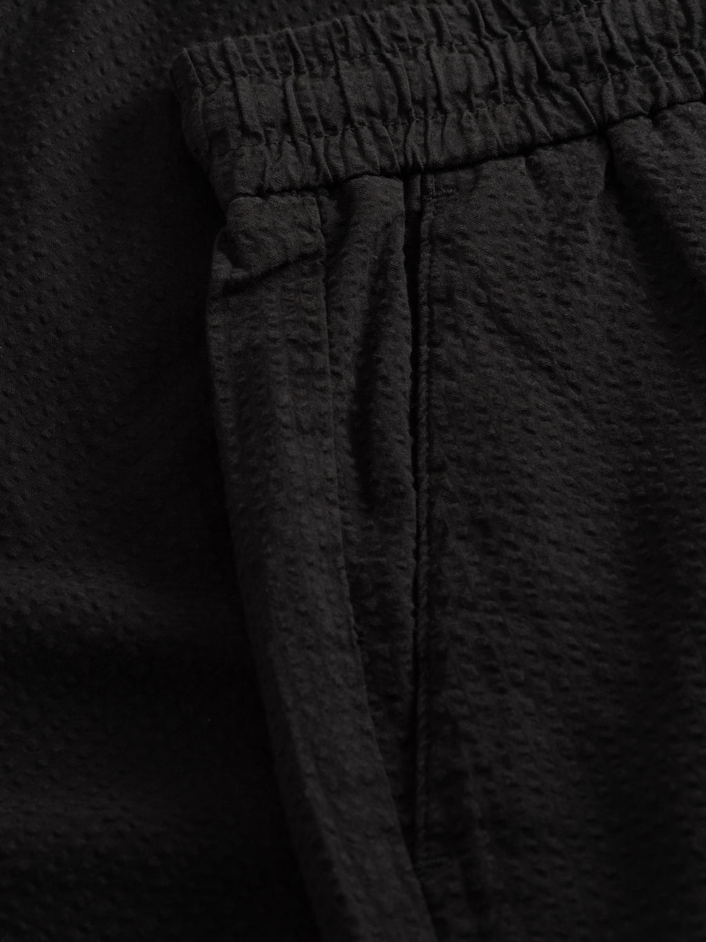 Close-up of Gabba GABtommi Ker Shorts - Black, featuring black textured fabric, elasticated waistband, side seam pocket, and a subtle dimpled pattern for stylish comfort in a regular fit.