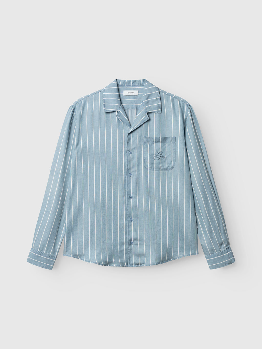 The Gabba GABtimo Resort Stripes LS Shirt in light blue denim features white vertical stripes, a pointed collar, and a left chest pocket. The shirt is shown laid flat on a white background.
