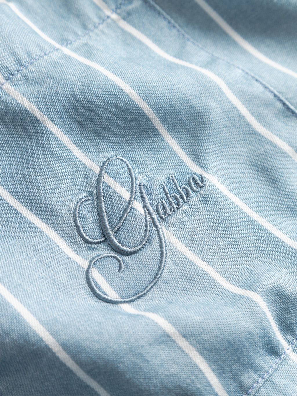 The GABtimo Resort Stripes LS Shirt by Gabba features light blue denim with thin white vertical stripes and “Gabba” elegantly embroidered in matching blue thread.
