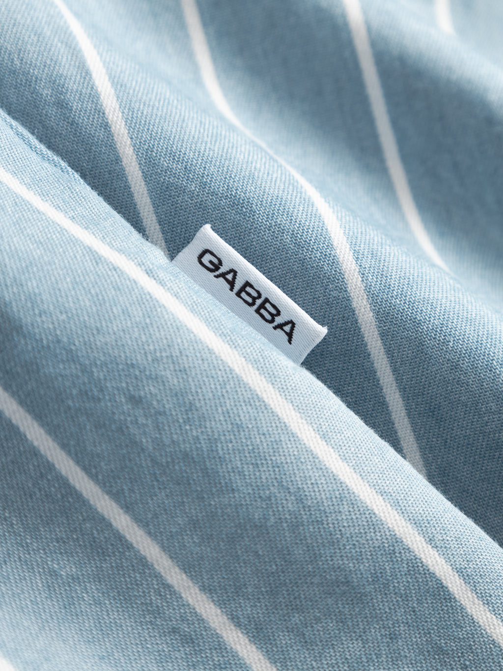 A close-up of the Gabba GABtimo Resort Stripes LS Shirt in light blue denim, featuring white diagonal stripes and a small white tag with 
