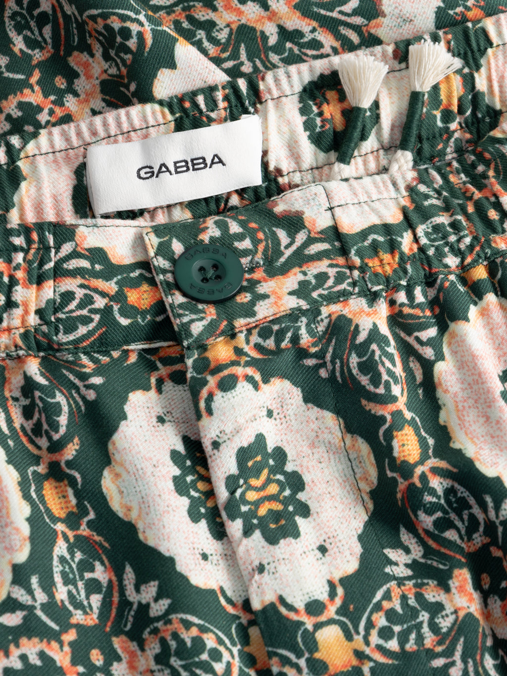 Close-up of the Gabba GABtommi Oro Shorts in a green pattern, featuring a green button, white drawstrings, elasticated waistband, and a visible brand label above the waistband.