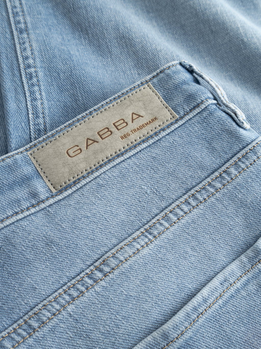 Close-up of GABmarc Hobok Jeans in mid blue denim by Gabba, highlighting the stitched leather label with GABBA REG. TRADEMARK on the waistband above the back pocket.