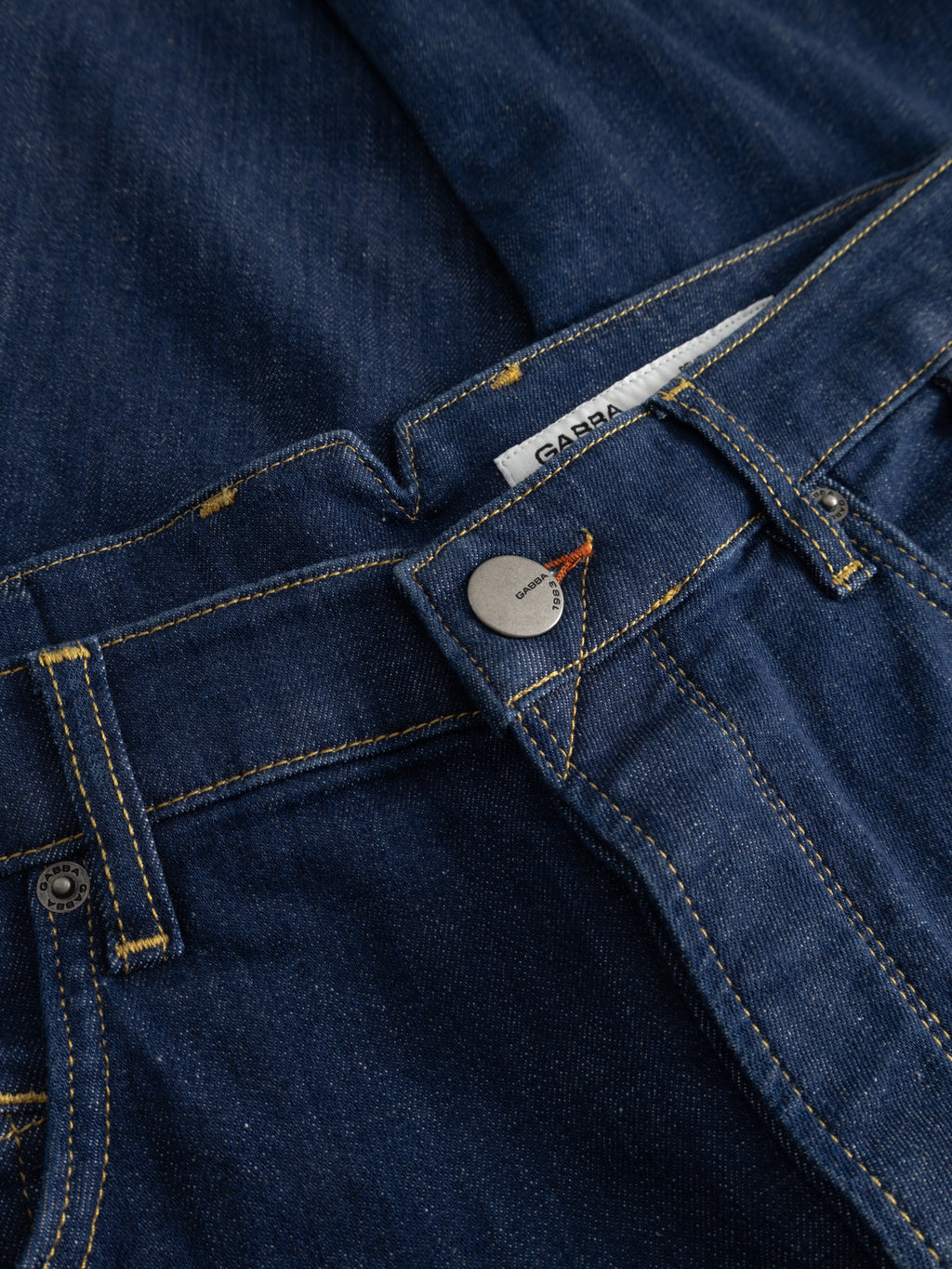 Close-up of premium dark denim GABalex SX Cropped Jeans by Gabba, featuring a visible metal button, yellow stitching, and a partially unbuttoned waist that reveals a white label with the Gabba brand name.