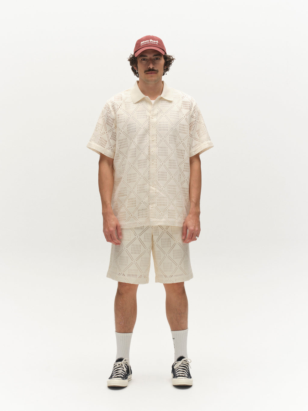 A man with a mustache models the Gabba GABsteven Croch SS Shirt GRS in Birch, paired with matching shorts, a red cap, white socks, and black sneakers, standing against a plain white background.