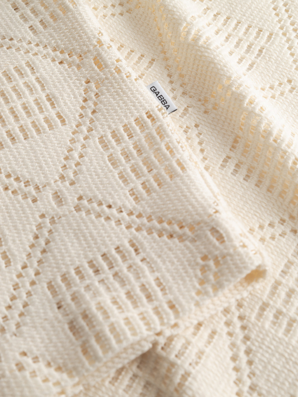 A close-up of the GABsteven Croch SS Shirt GRS in Birch by Gabba, showing cream textured fabric with a geometric cut-out pattern and a small sewn-on Gabba label.