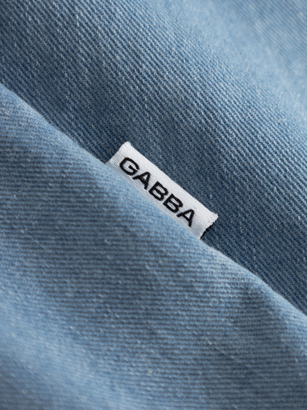 A close-up of the GABtimo Resort Denim SS Shirt in light denim blue by Gabba shows a white tag labeled 