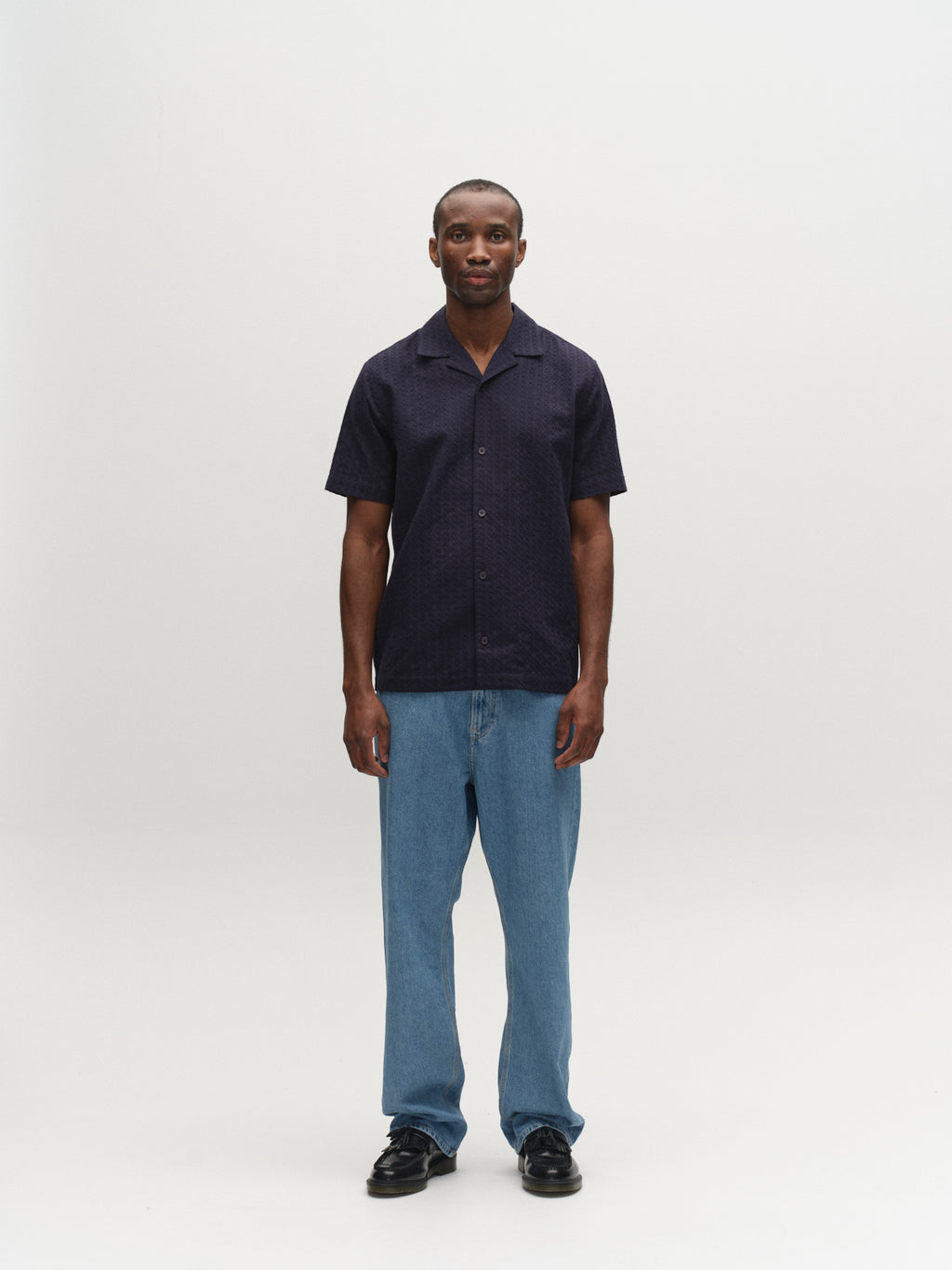A man faces forward against a plain white background, wearing the Gabba GABtimo Resort Neal SS Shirt in navy, light blue jeans, and black shoes.