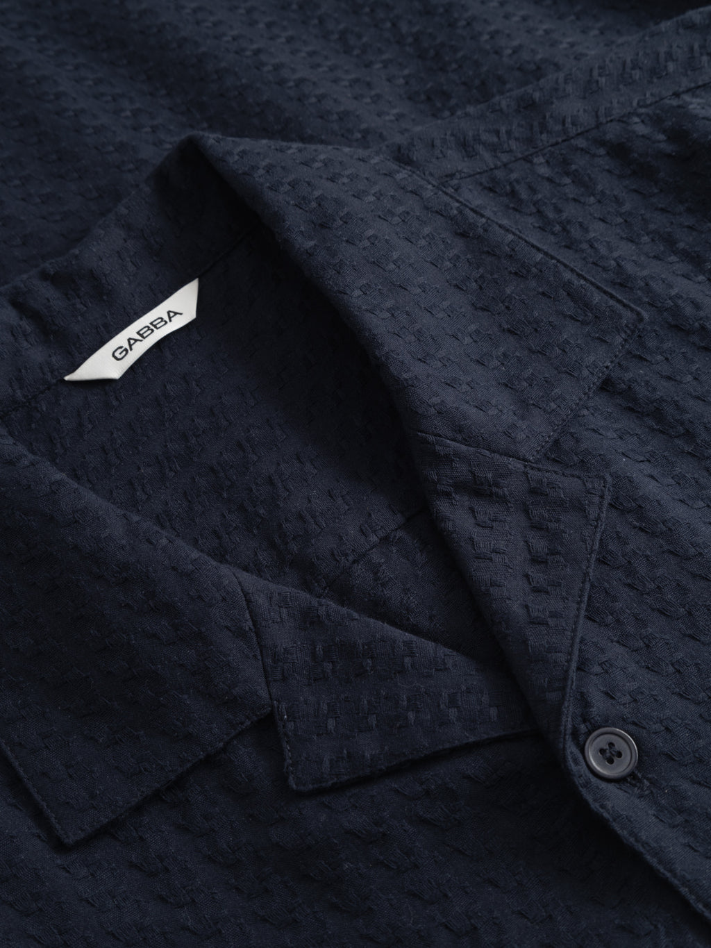 Close-up of the GABtimo Resort Neal SS Shirt in navy by Gabba, featuring a textured fabric, pointed collar, single black button, and a visible white label with the brand name.