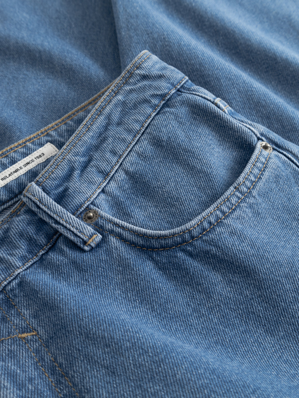 Close-up of Gabba GABmax 5poc Mid Jeans in mid blue denim, highlighting the front pocket, detailed stitching, and cotton fabric texture with a white tag partly visible inside the waistband.