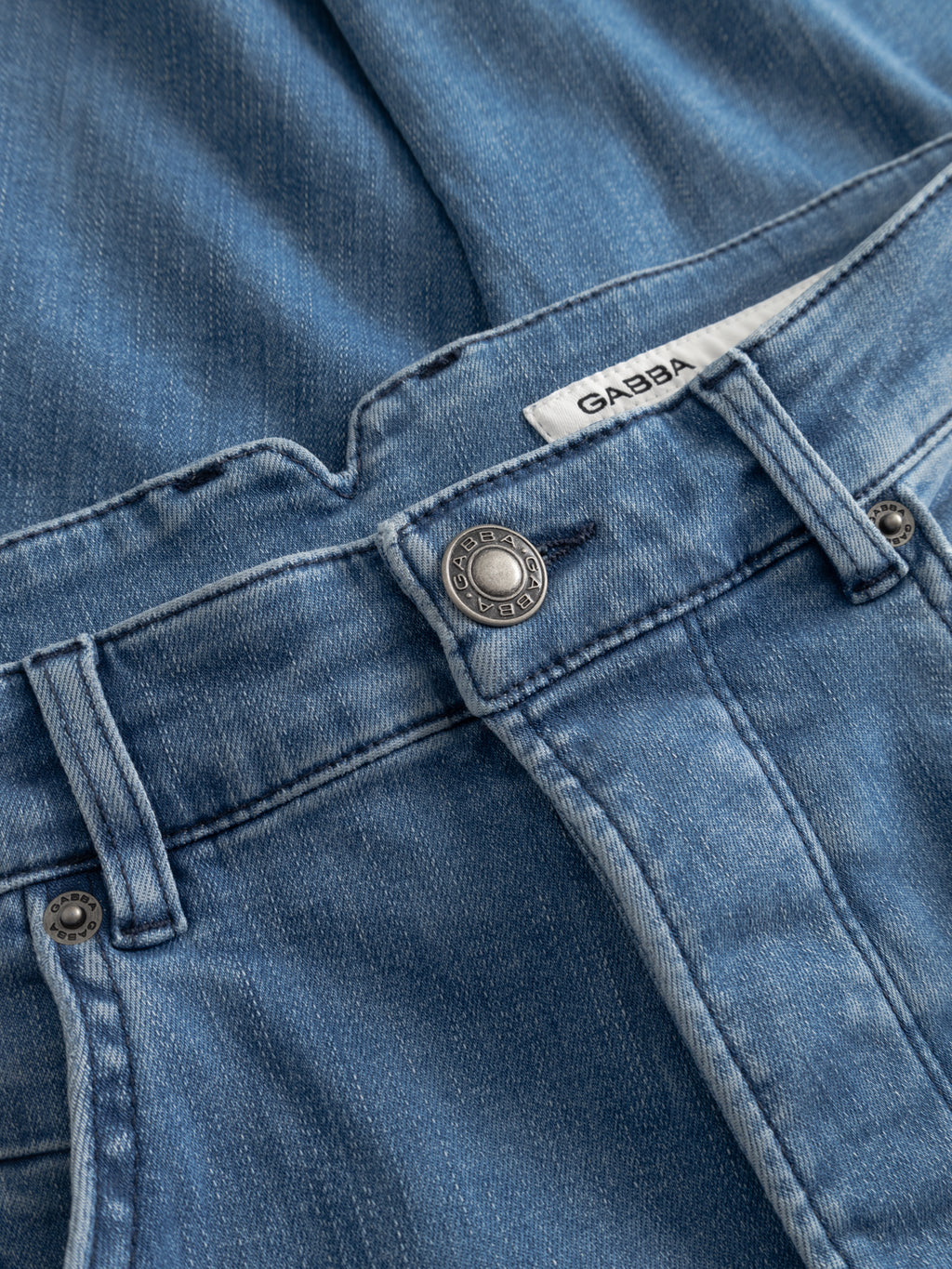 Close-up of Gabba’s GABalex Dhera Cropped Jeans in light blue super-stretch denim, showing the waistband, button, belt loops, and a white Gabba label with visible texture and stitching.