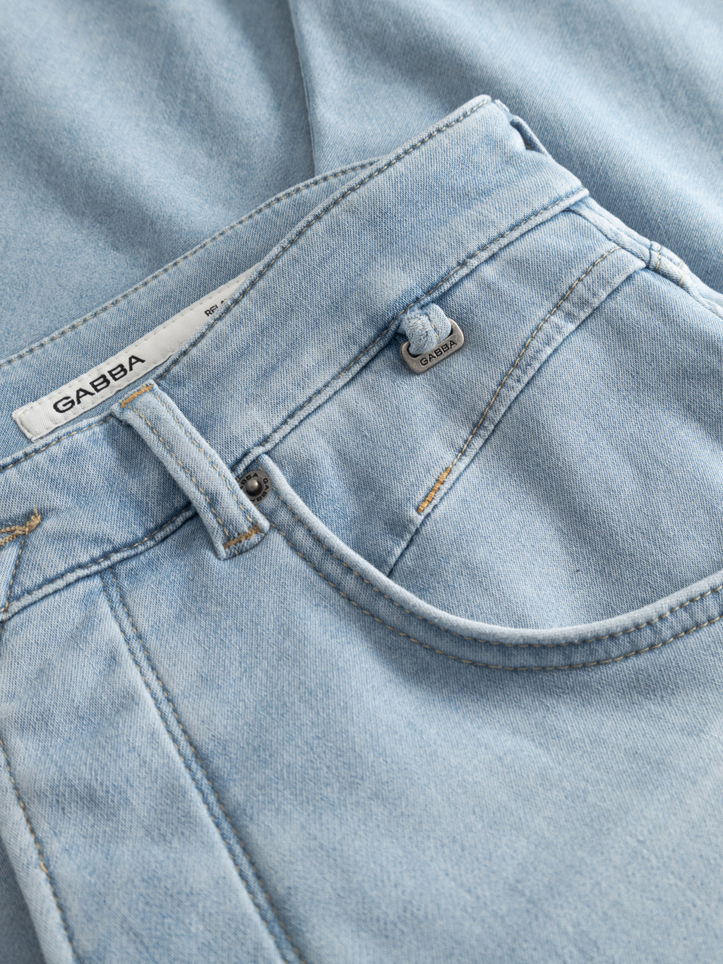 Close-up of GABalex Dynamic Cropped Jeans in light blue denim by Gabba, featuring comfort-stretch fabric, visible stitching, front pocket, belt loop, small metal tag, and a white inner waistband label with the Gabba brand name.