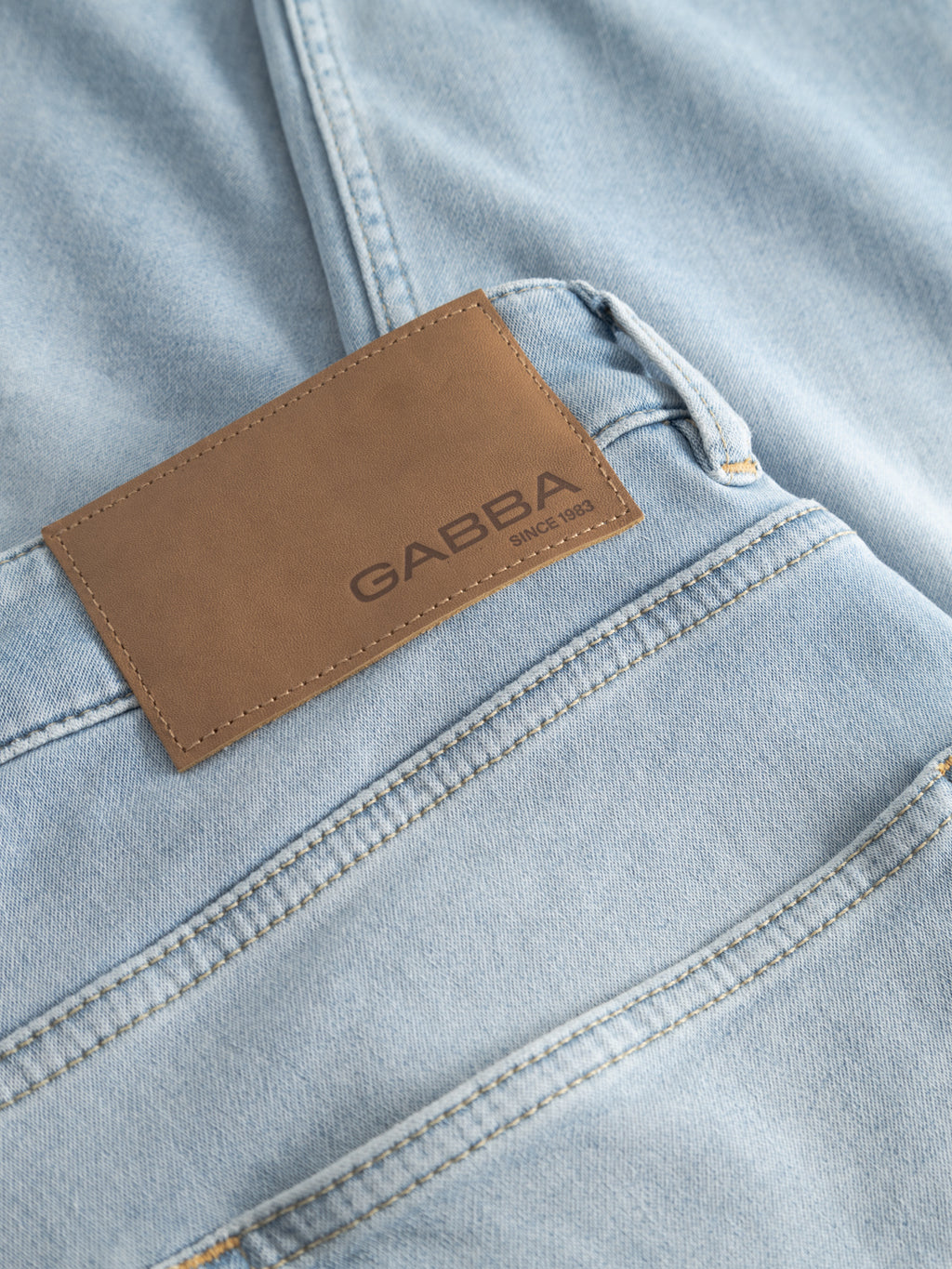 Close-up of GABalex Dynamic Cropped Jeans in light blue denim by Gabba, featuring a brown leather waistband patch with the brand’s name and “Since 1983.” Stitching and comfort-stretch fabric are visible.
