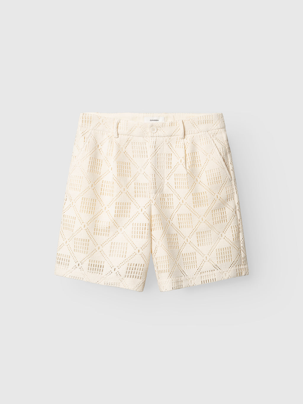 The Gabba GABjoli Ted Croch Shorts GRS - Birch are cream-colored chino shorts made from textured crochet fabric with a geometric cutout pattern, belt loops, and side pockets, shown on a plain light gray background.