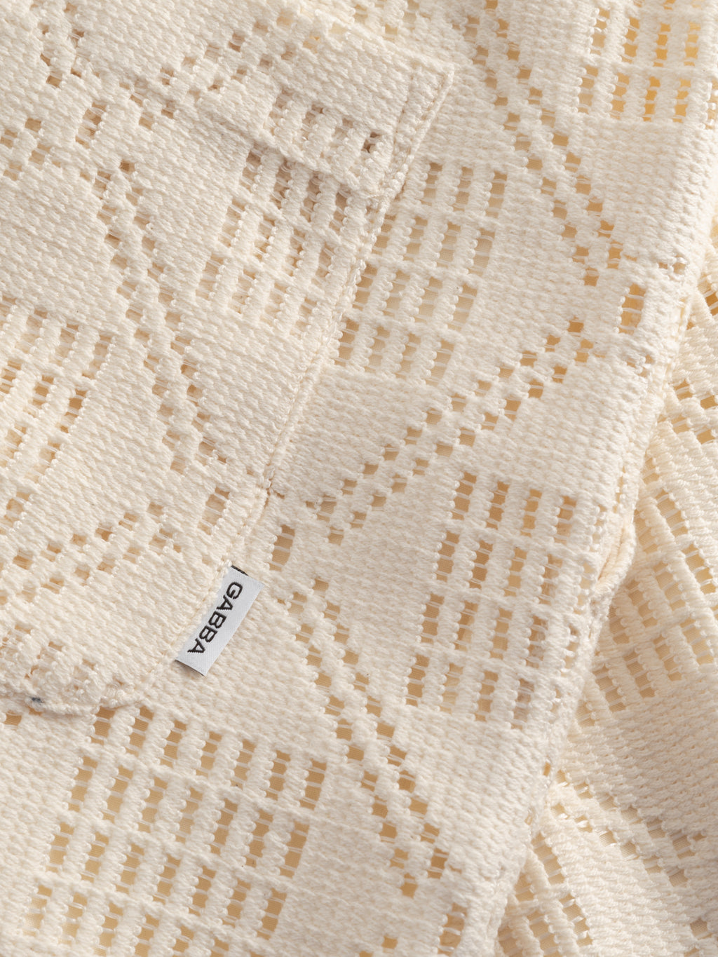 Close-up of the cream GABjoli Ted Croch Shorts GRS by Gabba, featuring textured crochet fabric with geometric cut-outs and a white Gabba label—ideal for relaxed summer style.