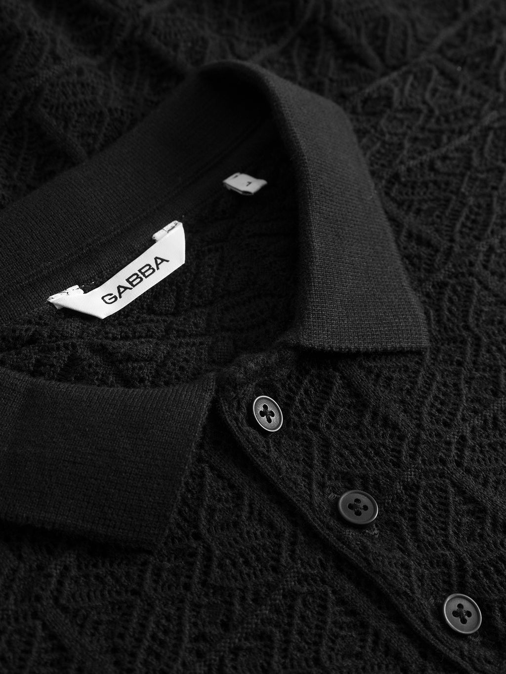 Close-up of the Gabba GABbenson Fiwi SS - Black polo shirt, featuring a black textured open knit pattern, buttoned placket, and an inner collar tag labeled Gabba.